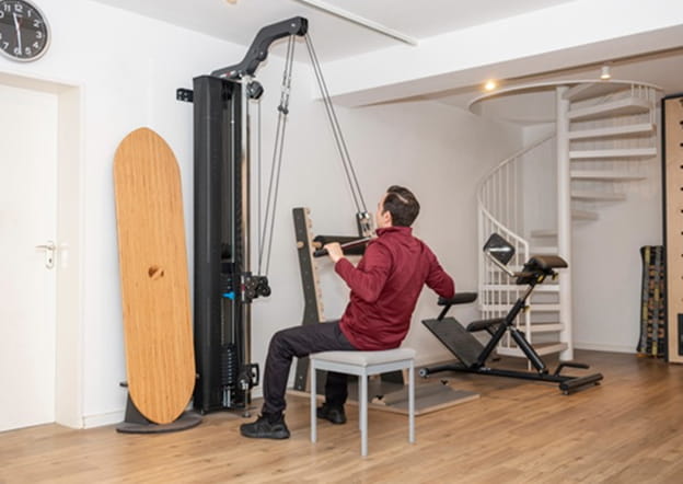 Patient trainiert am Seilzug mit Holzbrett an der Wand