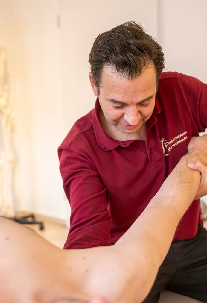Physiotherapeut behandelt die Schulter eines stehenden Patienten