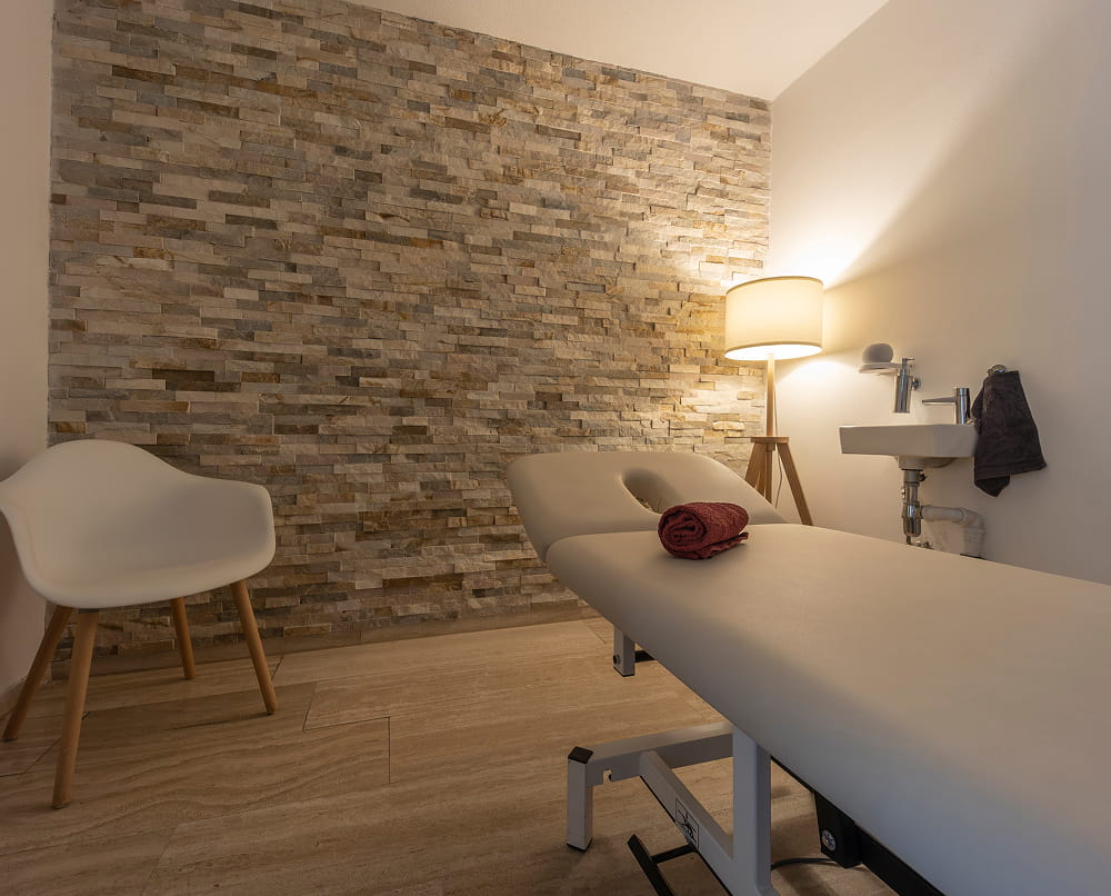 Behandlungsraum mit Natursteinwand und Therapieliege