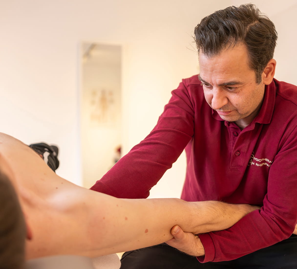 Physiotherapeut untersucht den Arm eines liegenden Patienten