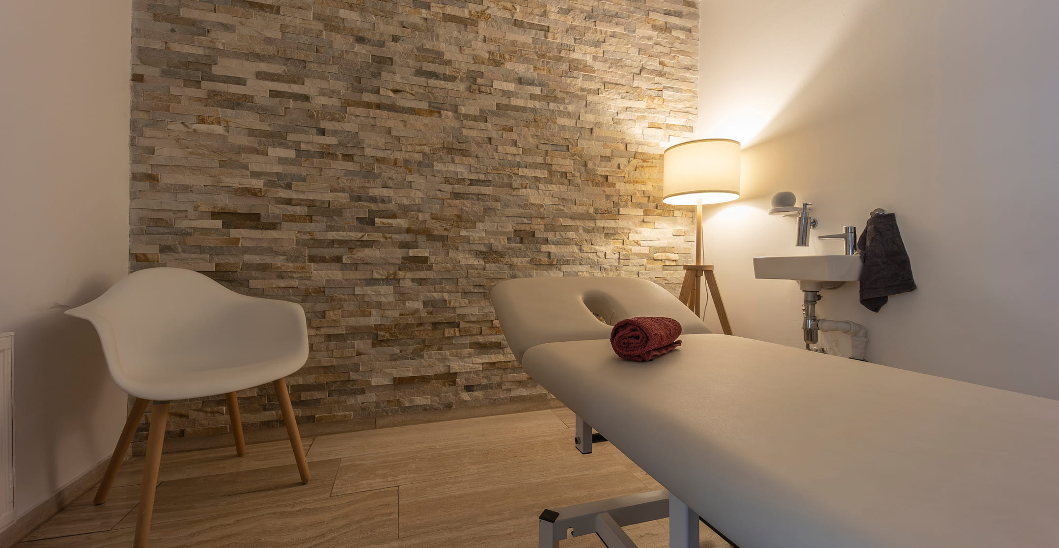 Behandlungsraum mit Natursteinwand und Therapieliege